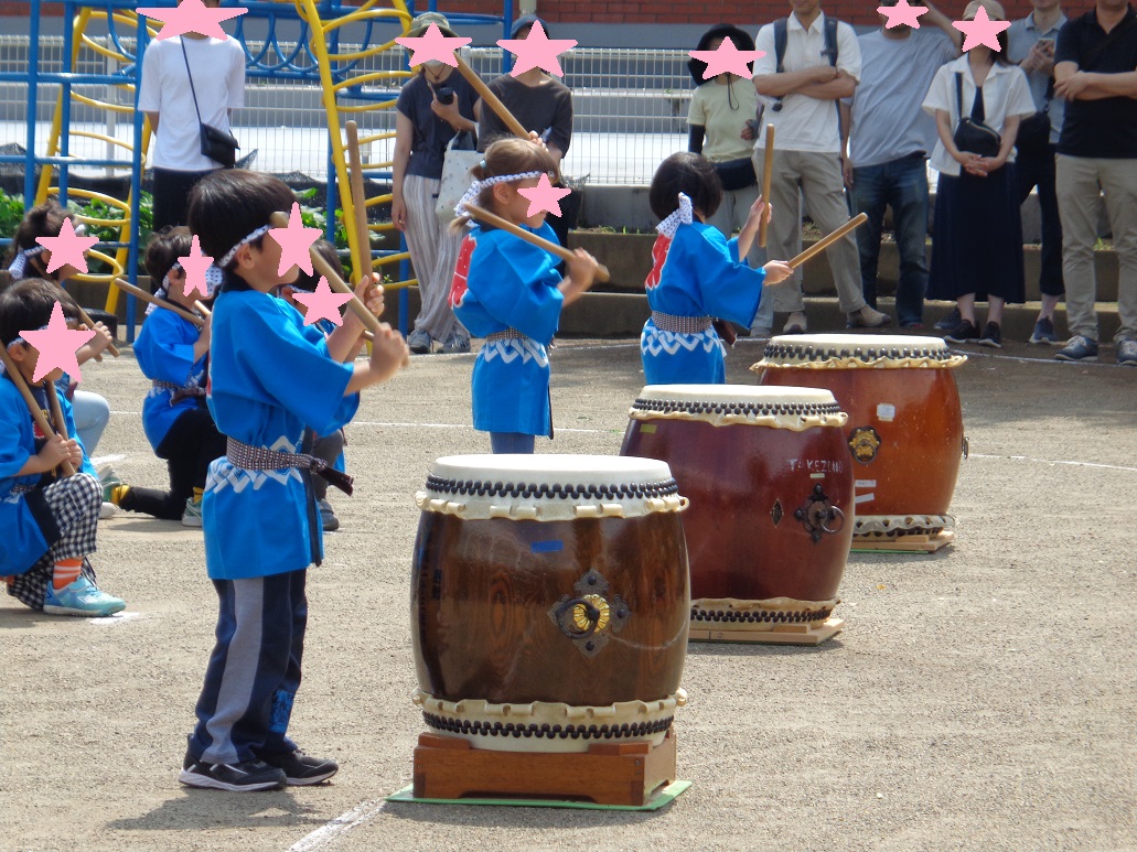 青色の法被を着て、両手にバチを持ち太鼓の前に立つ子どもたち