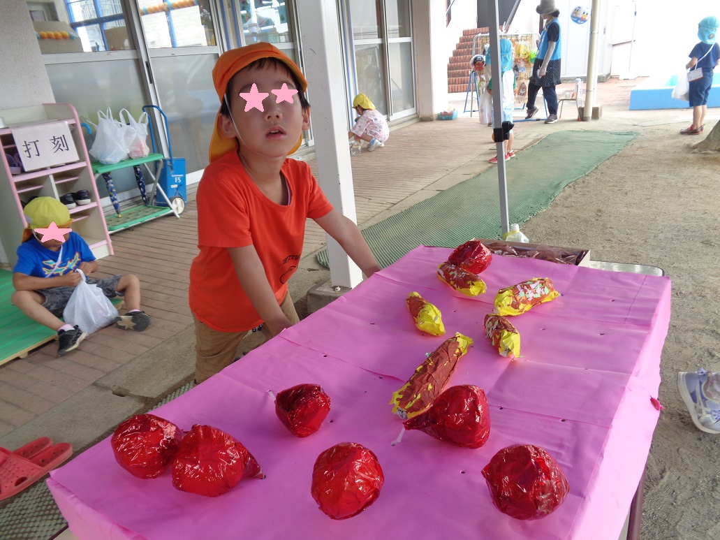 ピンク色のテーブルの上に赤や黄色の物を置き、子どもが立っている。