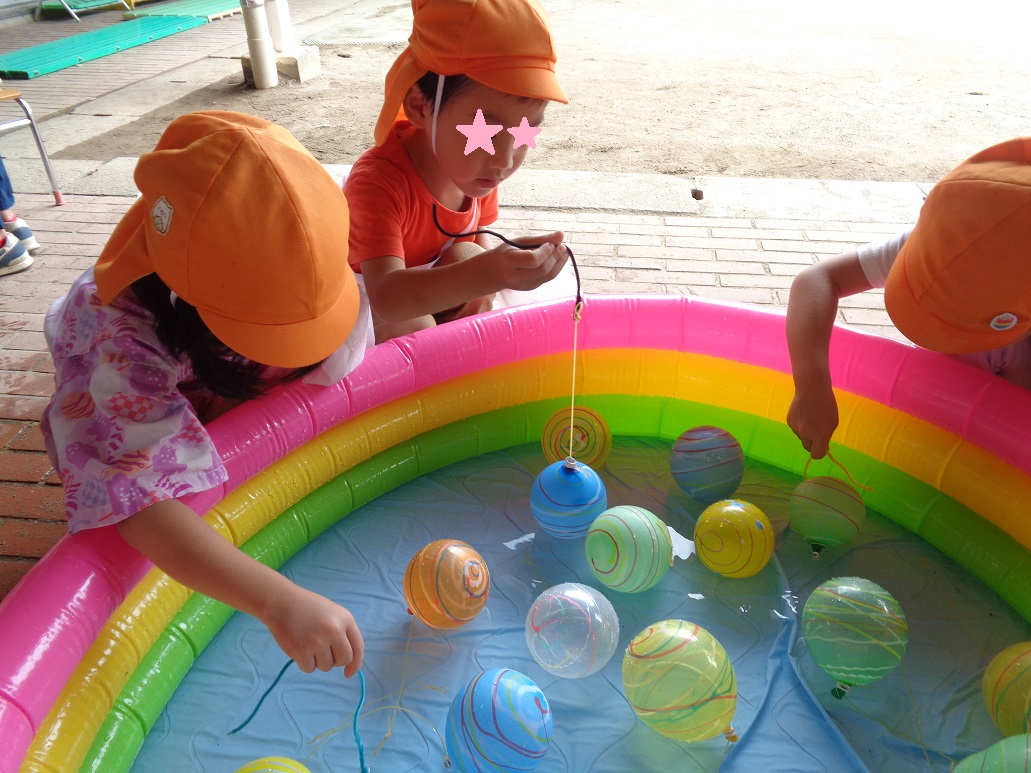 ビニールプールになかで水に浮かんだヨーヨーをひもで釣りあげようとする子供たち
