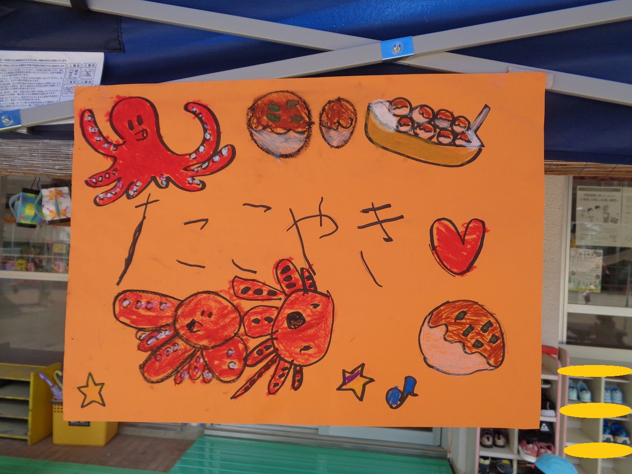 オレンジ色の画用紙にたこ焼きと平仮名で書いたり生き物のタコやたこ焼き、星の絵が描かれている。