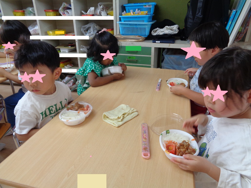 テーブルの周りに座りパックに入ったお弁当のふたを外そうとしている子どもたち