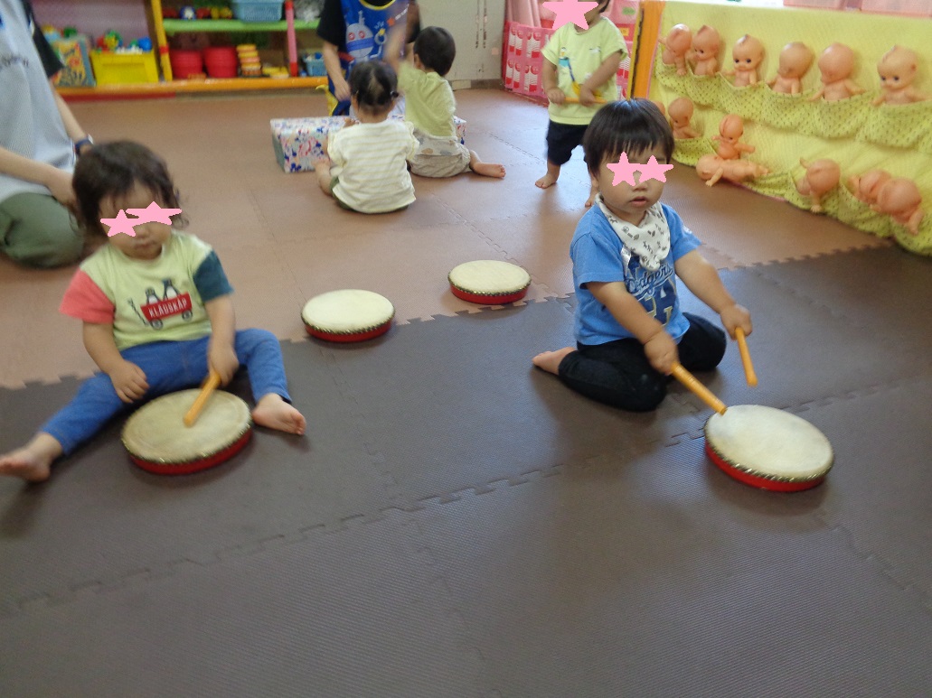 子どもたちが座って手に棒を持ち太鼓をたたいている