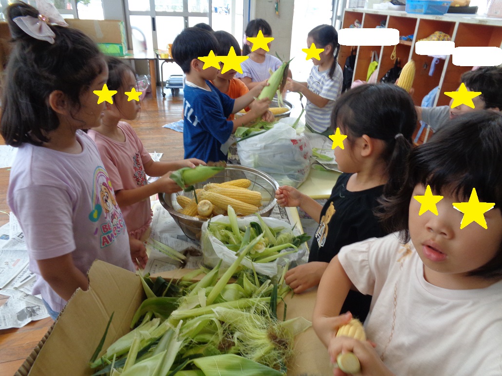 トウモロコシを手に持ち皮を子どもたちが剥き、段ボール箱の中に皮が入っている。
