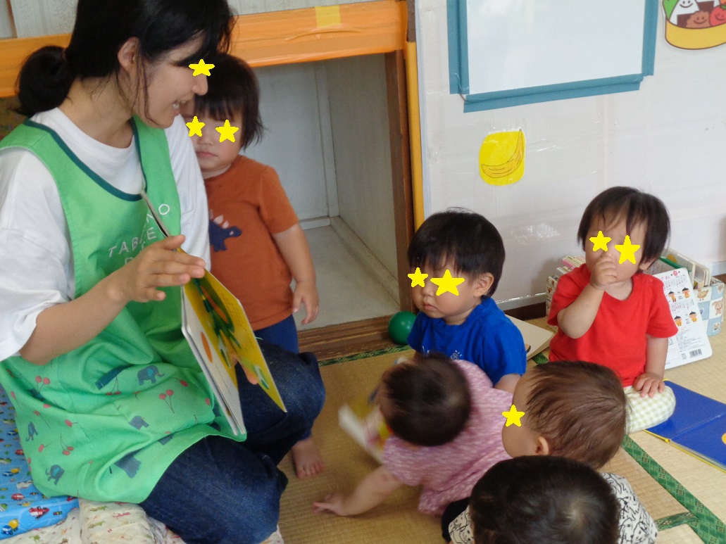 絵本を持っている大人の前に小さな子どもたちが座ってみている
