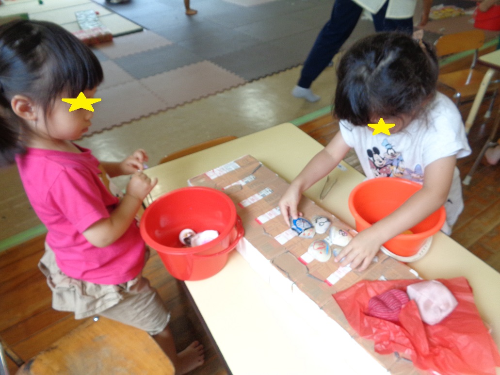 テーブルに赤いバケツや白い貝やお手玉を並べている子どもたち