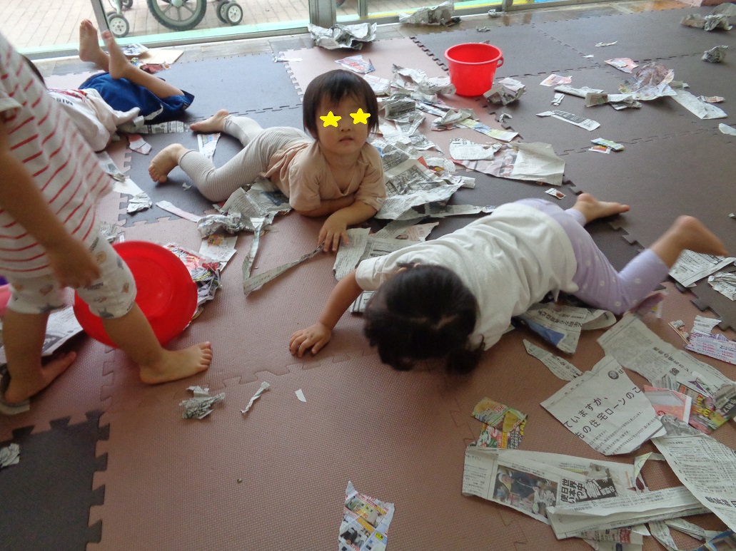 破いた新聞紙が床に広がり子どもが寝転んでいる