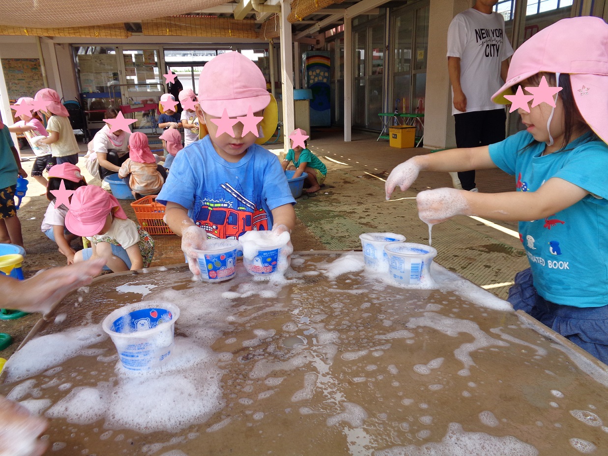 プラスチックのカップに泡を入れたり、手についた泡をテーブルの上に落としたり座っている子どもたち