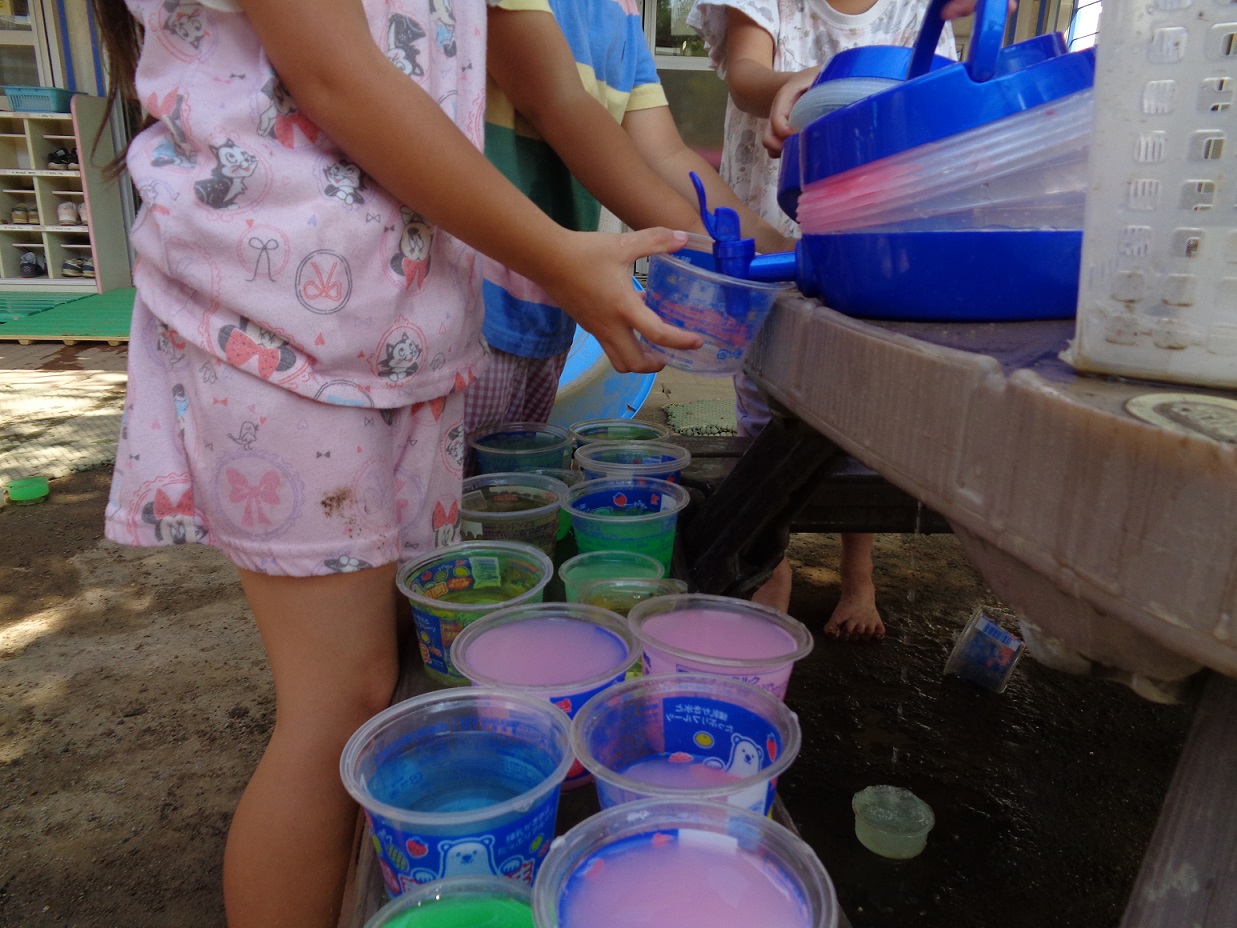 プラスチックのカップに色水を入れている子ども