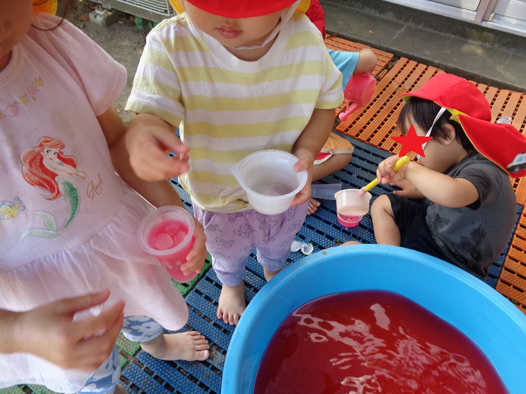 子どもたが小さいものと手につかんだりコップに赤い水を入れもち、水色のタライに赤い水が入っている