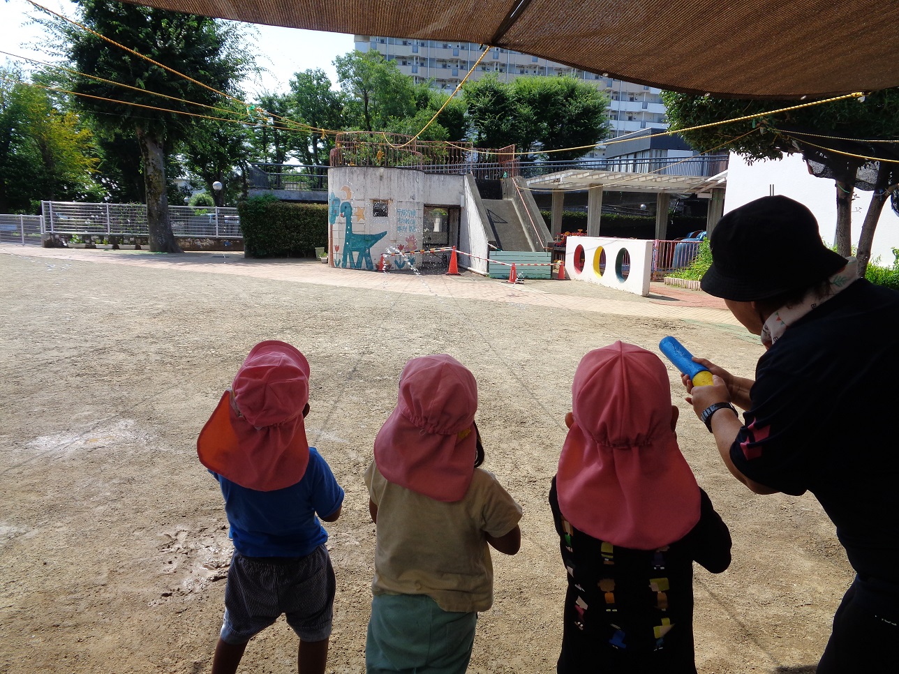 ピンク色の帽子をかぶった子どもたちが水鉄砲で水を飛ばしている