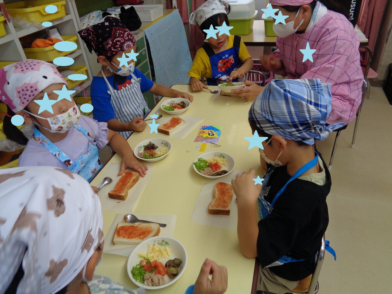 テーブルの上にパンとピザの具材を並べ、三角巾とエプロンを身に着けた子どもたちが作り始めた