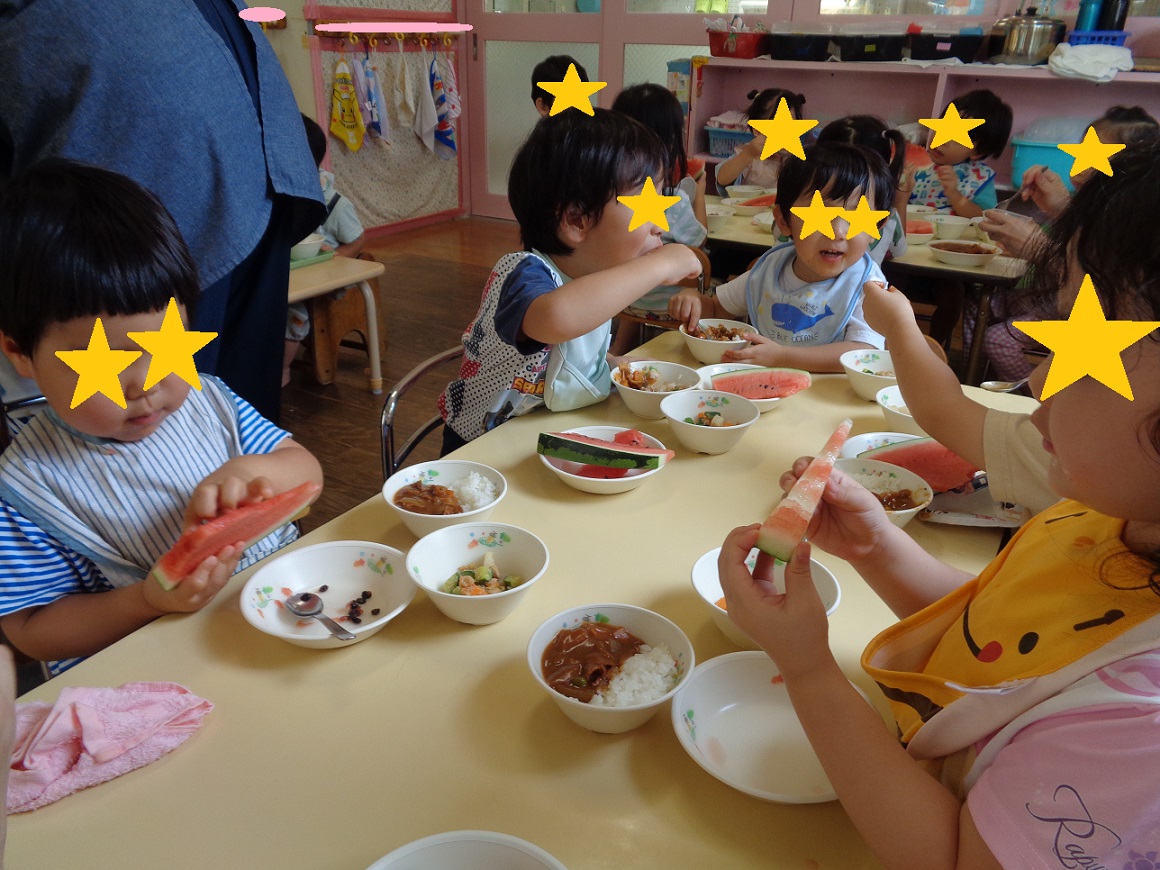 子どもたちが座って給食を食べてたりスイカを持っている