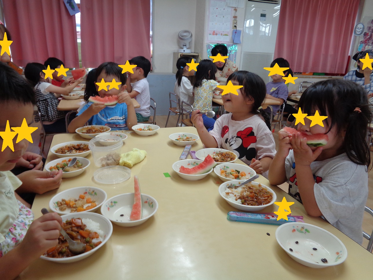 子どもたちが座ってスプーンを持ちハヤシライスを食べたりスイカを持ってたべている