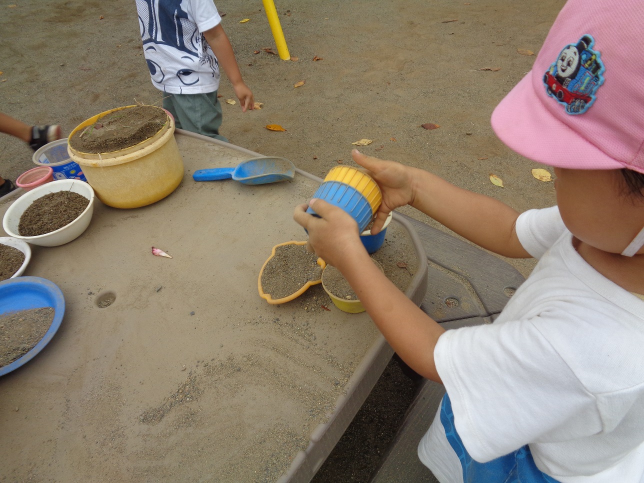 子どもがカップを持って砂遊びをしている