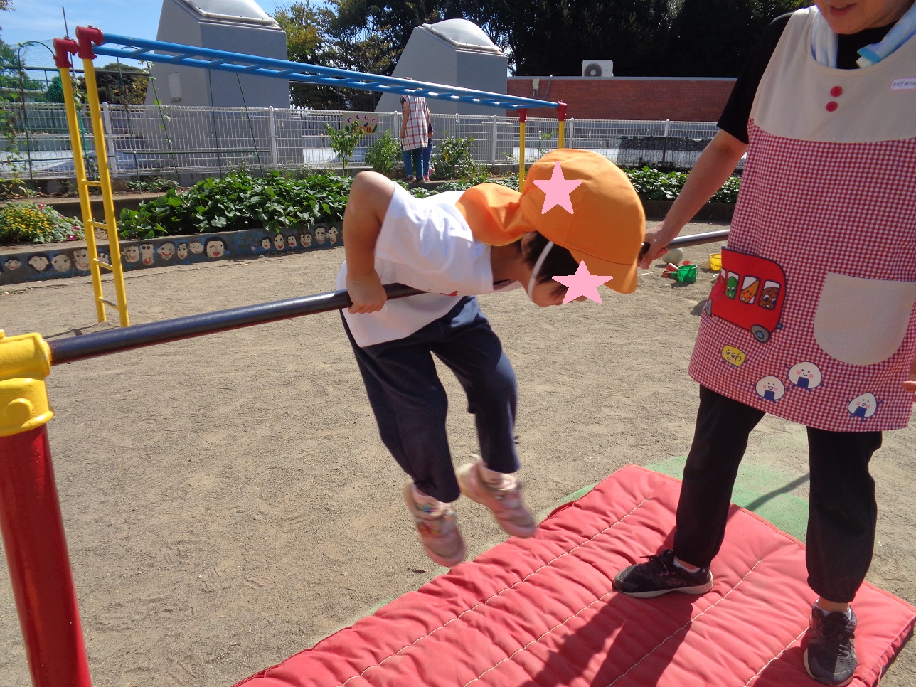 子どもが鉄棒にお腹を付けて登ったところをおとながみている