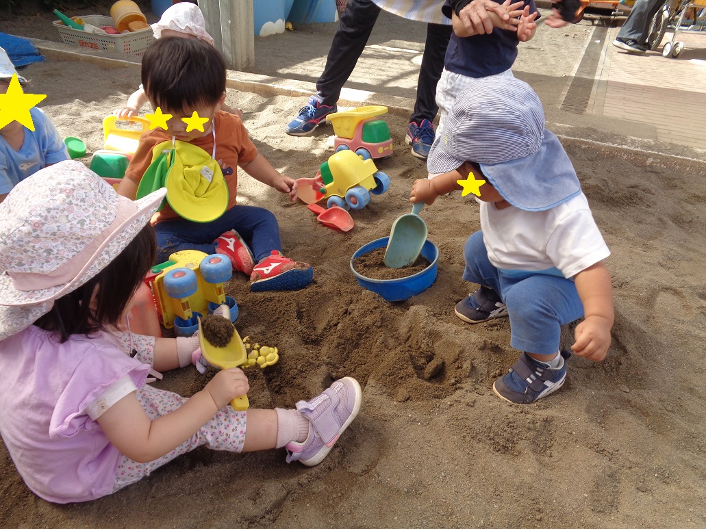 砂場に座った子どもがシャベルで砂をすくっている