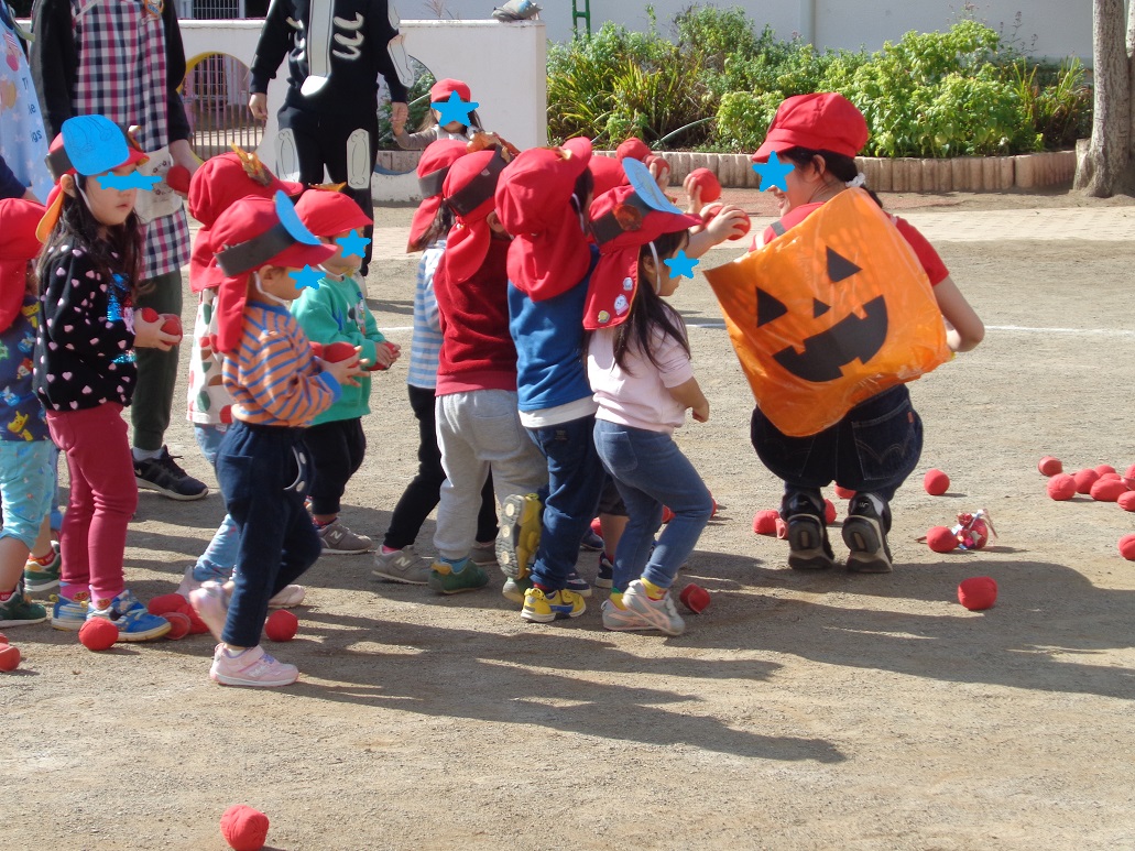 赤い帽子とおばけのお面を付けた子どもたちが赤い玉をかぼちゃのおばけの籠に向かって投げている