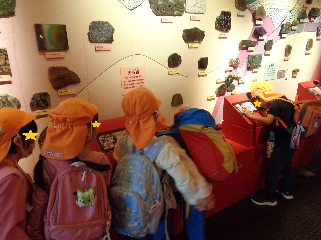 オレンジ色の帽子を被った子どもたちが展示してある石を見ている。