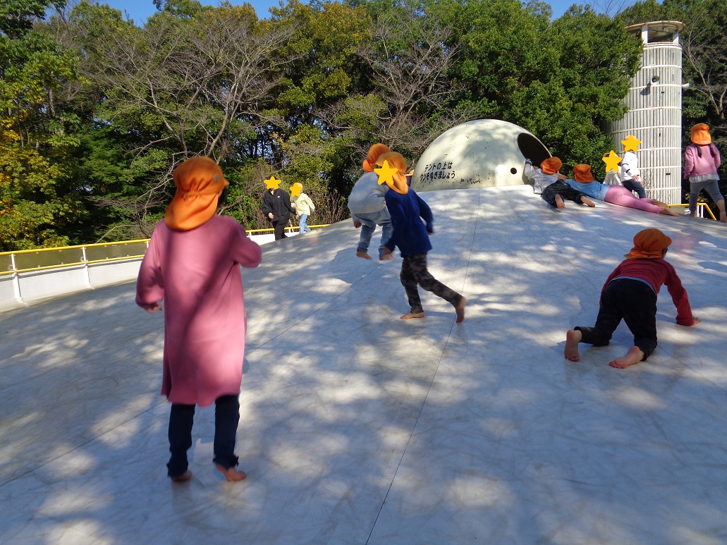 白い大きなトランポリンでオレンジ色の帽子の子どもたちが遊んでいる。