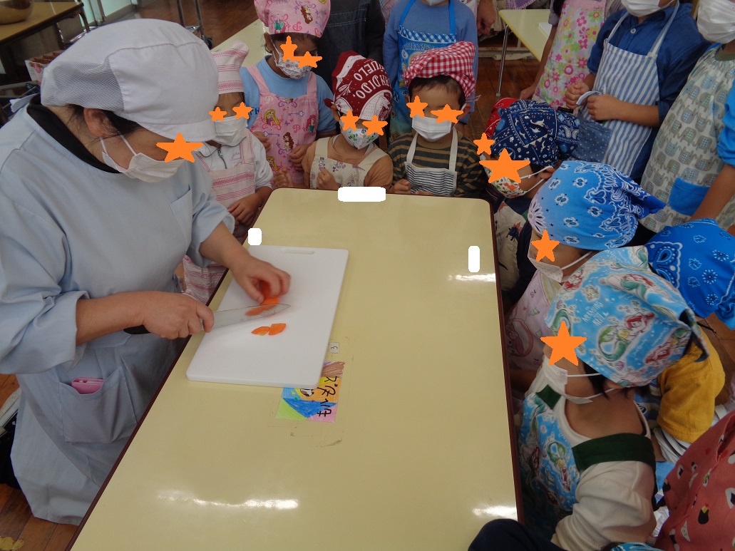 大人が人参を包丁で切るところを子どもたちが見ている