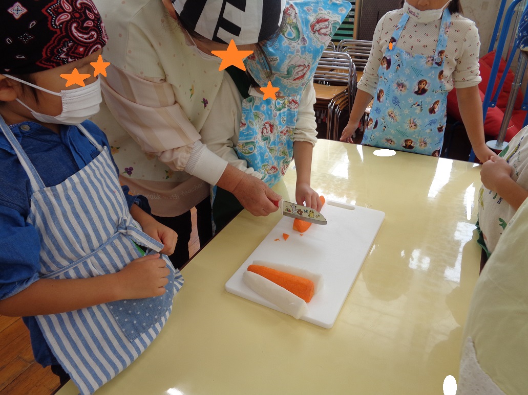 保育士が補助しながら子どもが人参を包丁で切ろうとしている