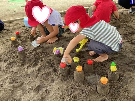 カップに砂を入れフルーツの玩具をのせケーキにする3歳児