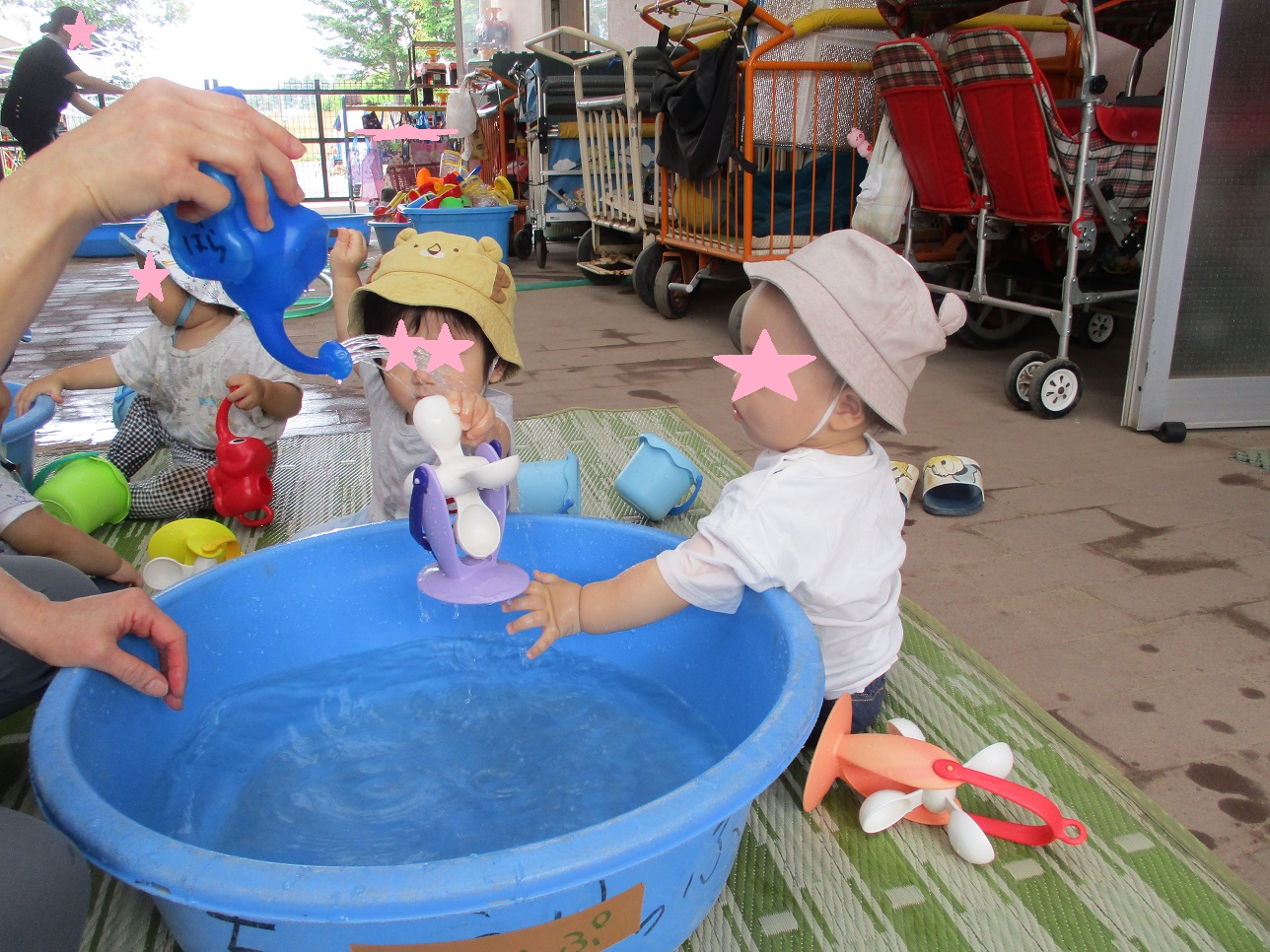 ジョーロから水がおちそれを触ろうとする子供が手を伸ばしたり見ている