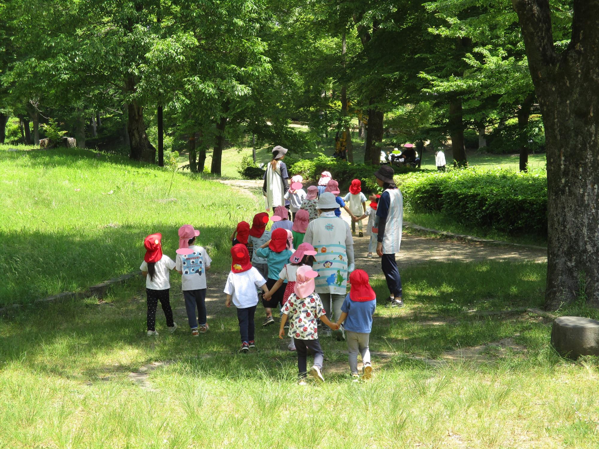 木々のある公園で子どもと大人が散策をしている