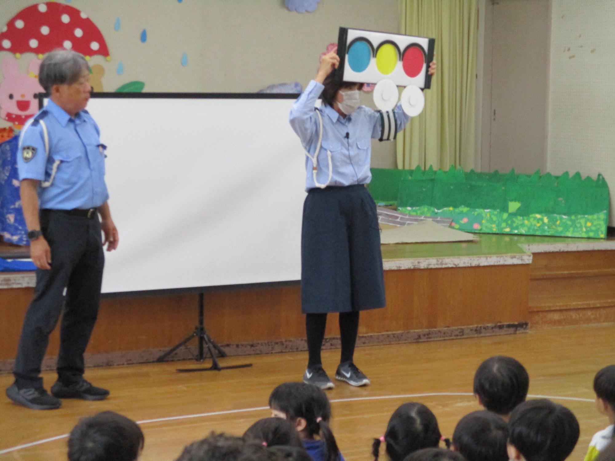 交通安全協会の方が3色の信号のボードを持ち見る子供たち