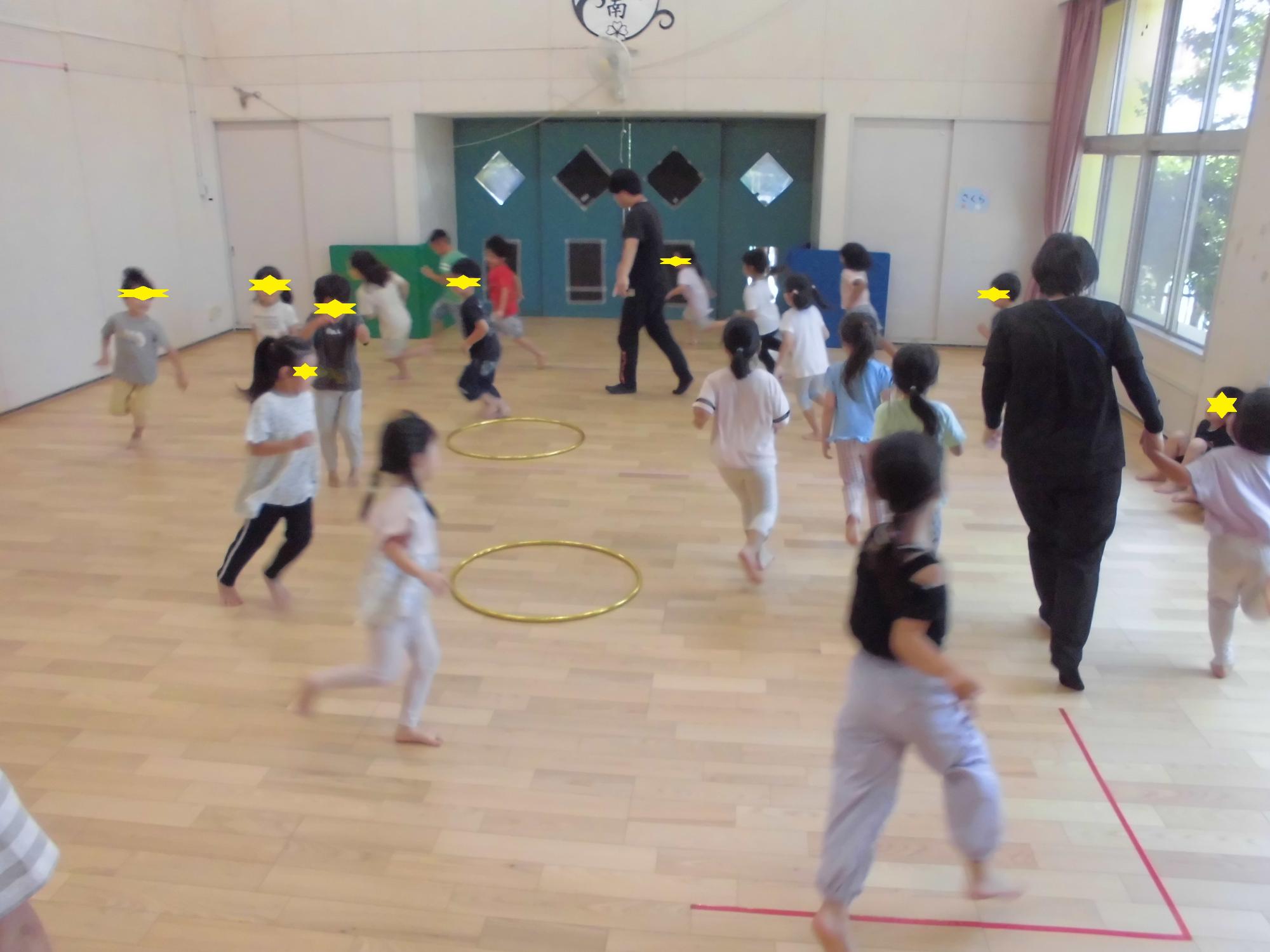 小学校の先生と年長児がホールでフープ取りゲーム